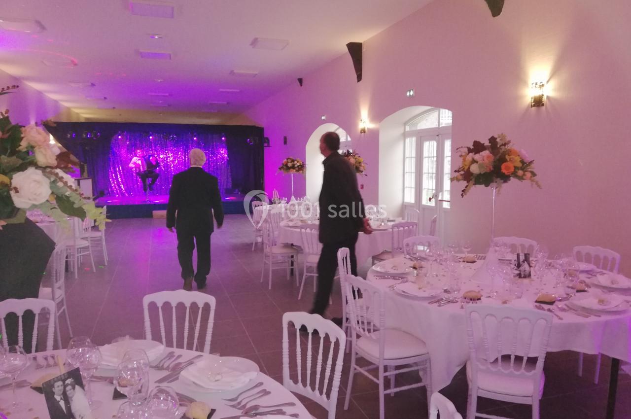 Salle de réception décorée avec des tables dressées, des fleurs et une scène illuminée en arrière-plan.