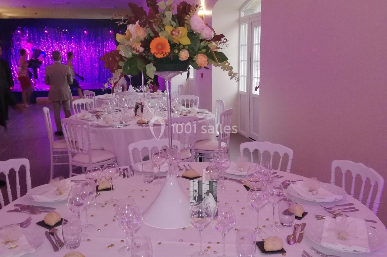 Salle de réception décorée avec des tables rondes élégantes, nappes blanches et centre de table floral.