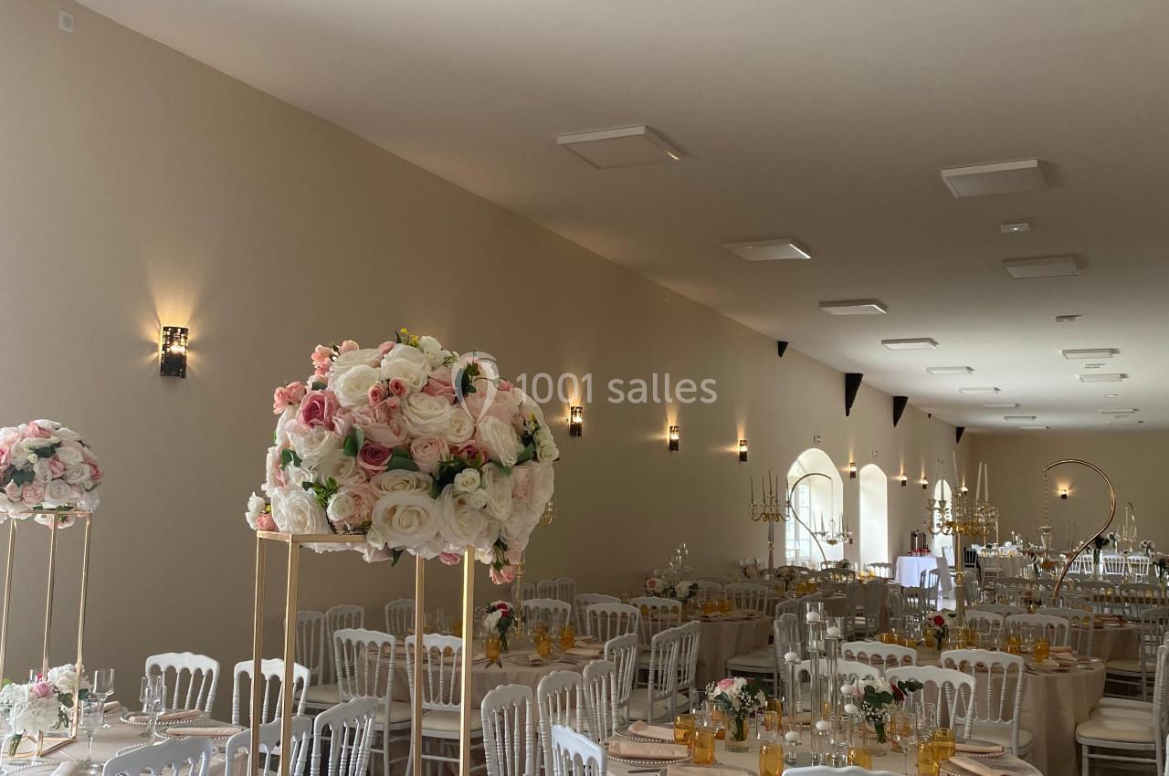 Salle de réception élégamment décorée avec des tables rondes, nappes blanches et centres de table fleuris.