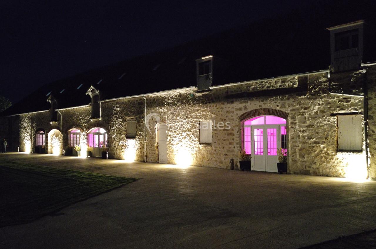 Façade d'un bâtiment en pierre éclairée la nuit avec des lumières jaunes et des fenêtres illuminées en rose.