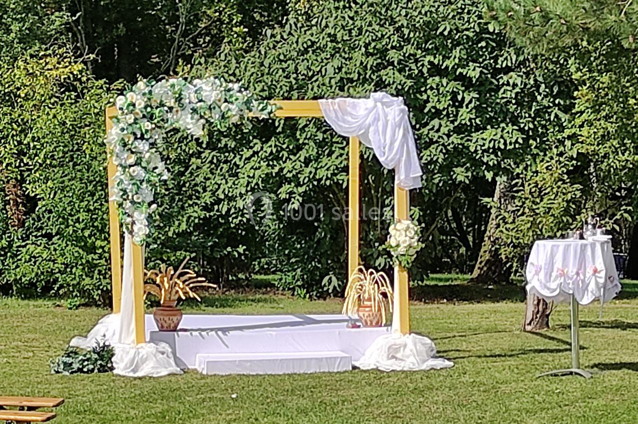 Arche de mariage décorée de fleurs blanches et de tissu, installée dans un jardin verdoyant.