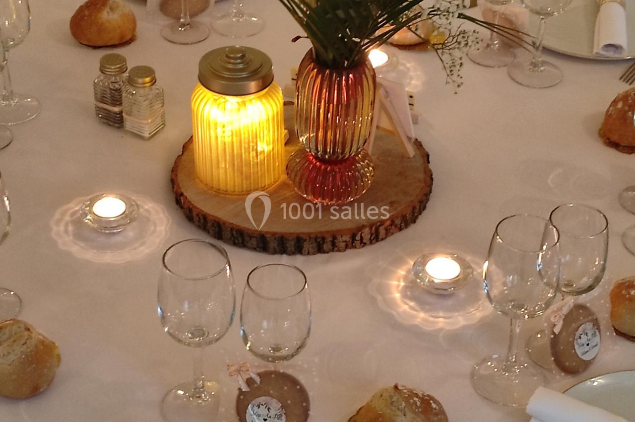 Table de réception décorée avec des bougies, des fleurs, des verres et des couverts dorés sur une nappe blanche.