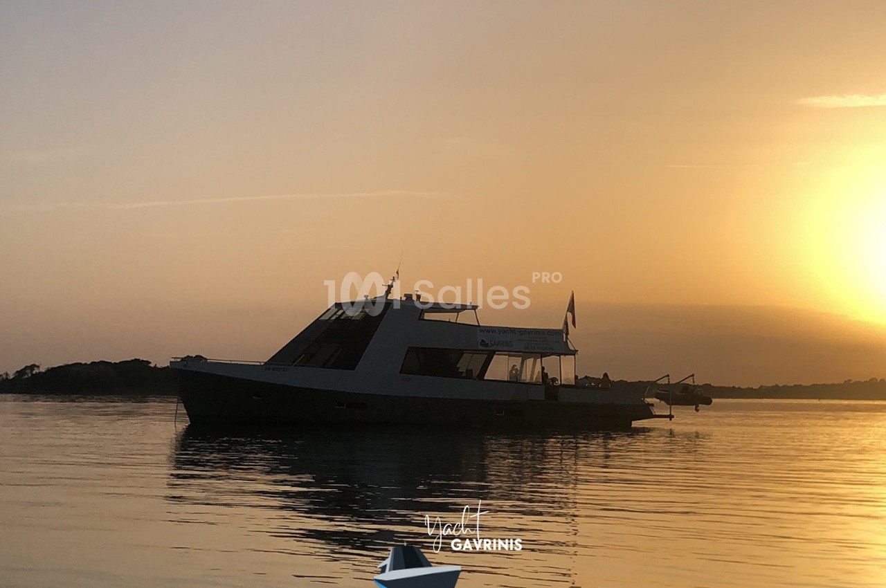 Bateau à moteur naviguant sur une eau calme au coucher du soleil, avec un ciel orangé en arrière-plan.