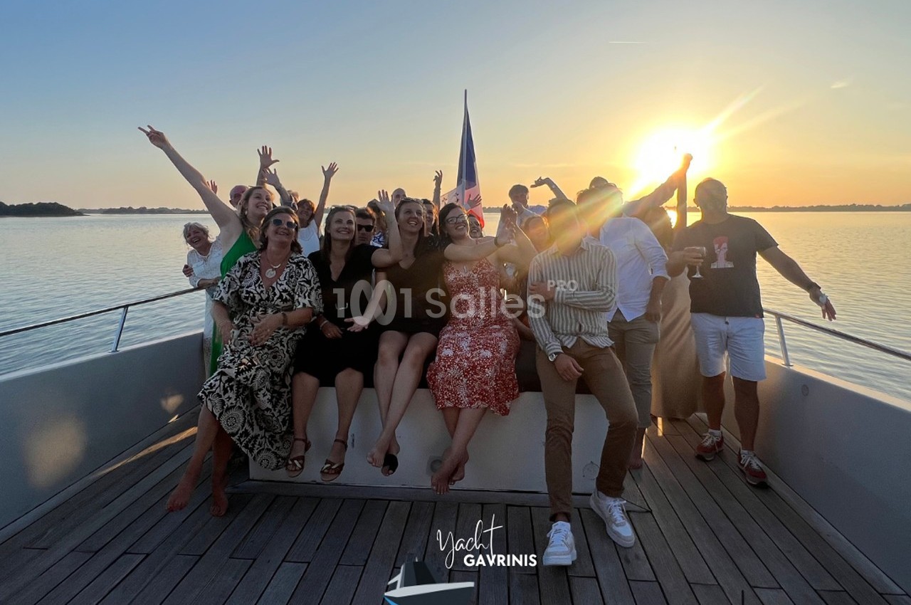 Un groupe de personnes souriantes posant sur le pont d'un bateau au coucher du soleil.