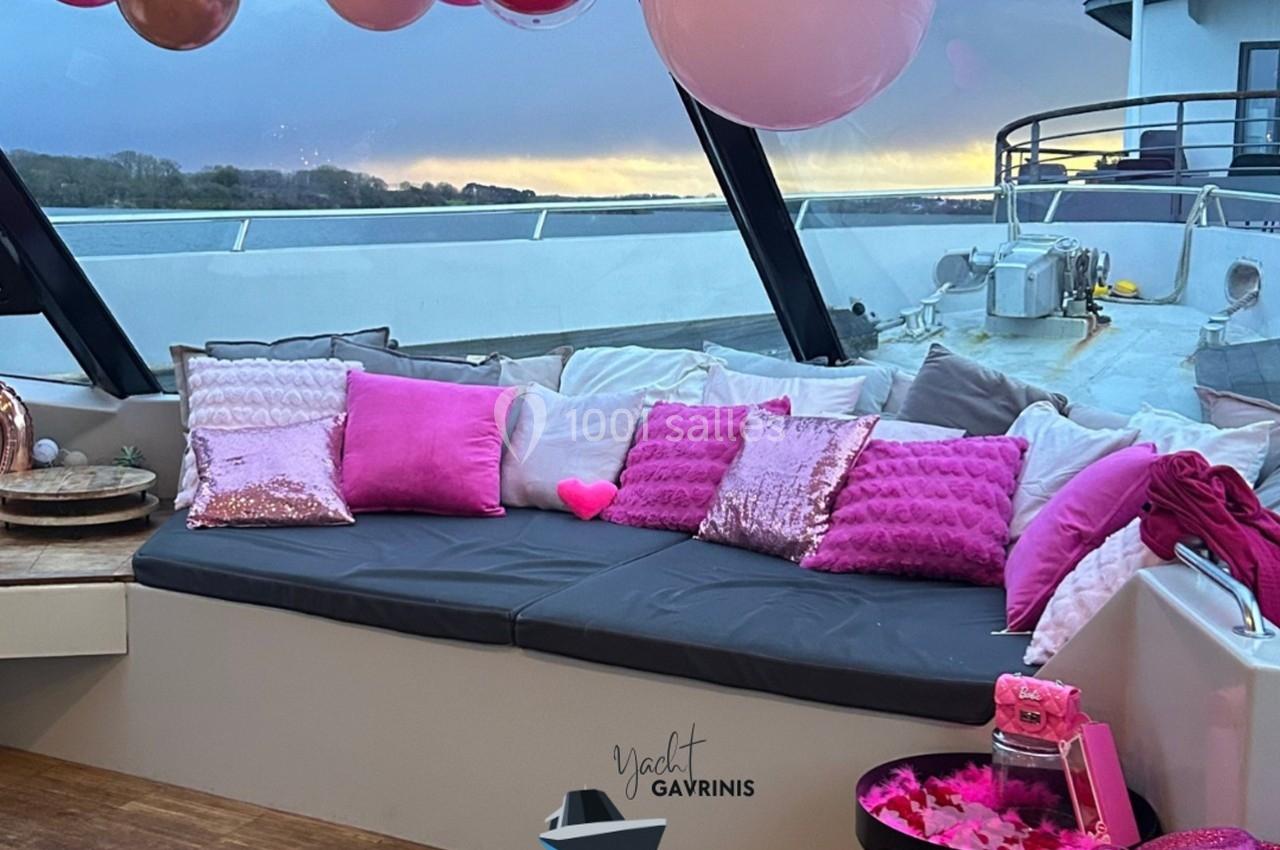 Banquette extérieure décorée de coussins roses et ballons, sur un yacht au coucher du soleil.