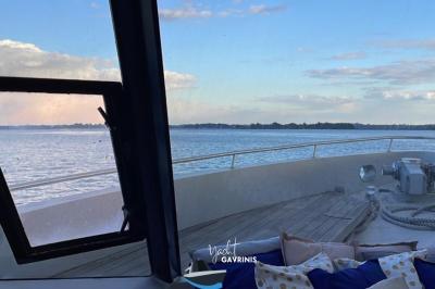 Mobilier en rotin noir avec coussins blancs sur une terrasse en bois couverte, vue sur l'extérieur urbain.