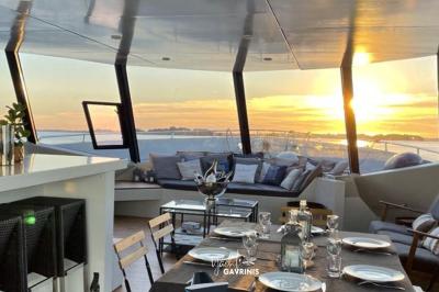 Mobilier en rotin noir avec coussins blancs sur une terrasse en bois couverte, vue sur l'extérieur urbain.