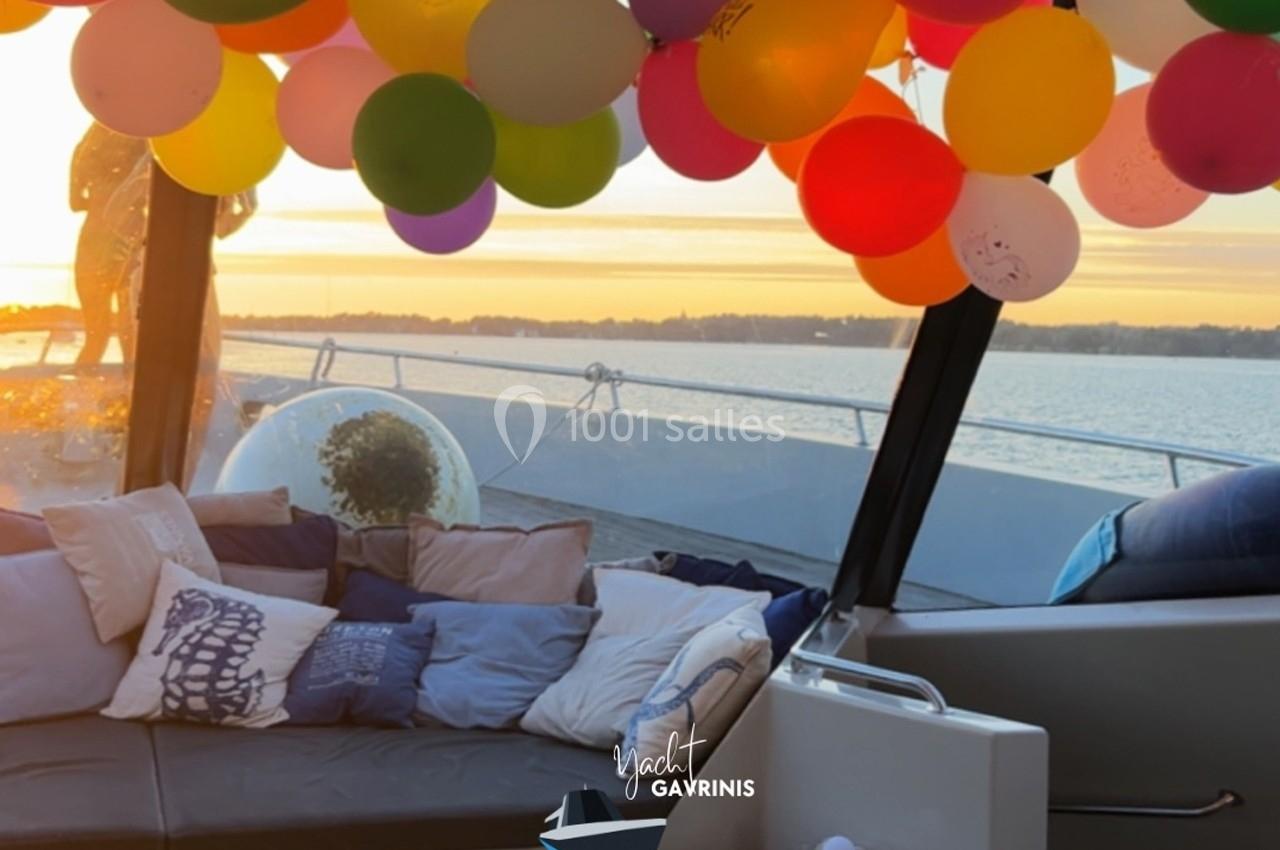 Intérieur d'un yacht décoré de ballons colorés, avec vue sur un coucher de soleil et un plan d'eau.