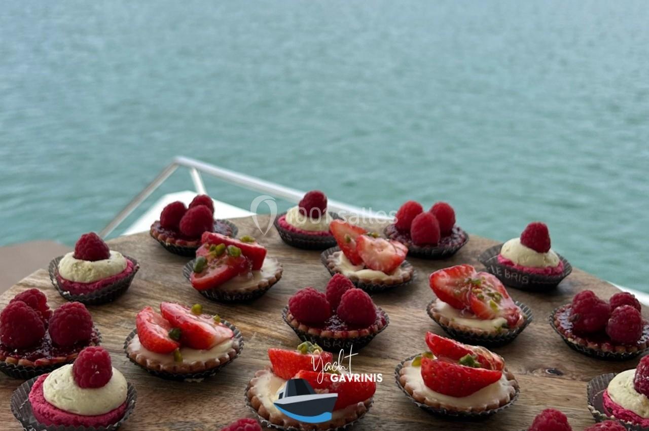 Plateau de mini-tartelettes garnies de fruits rouges, présenté sur un bateau avec vue sur une étendue d'eau.