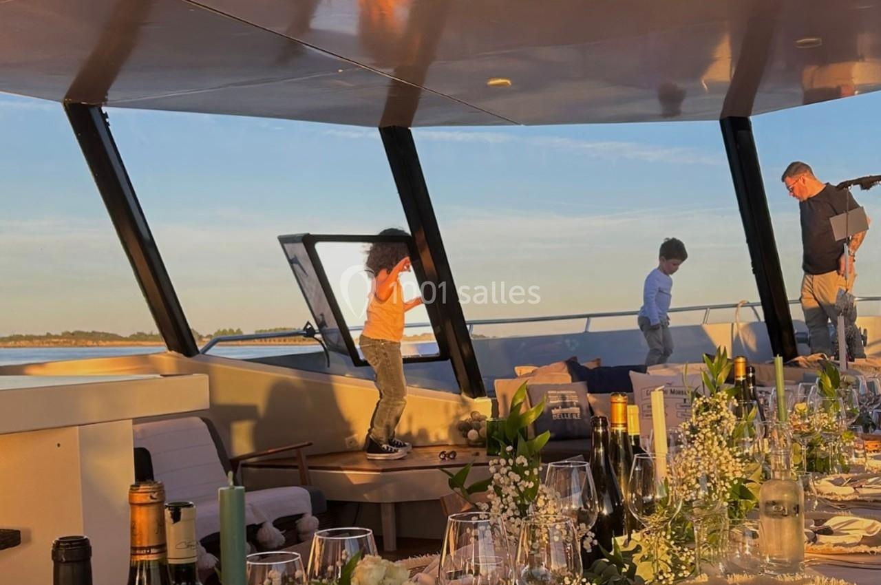 Deux enfants jouent sur le pont d'un bateau au coucher du soleil, avec une table dressée au premier plan.
