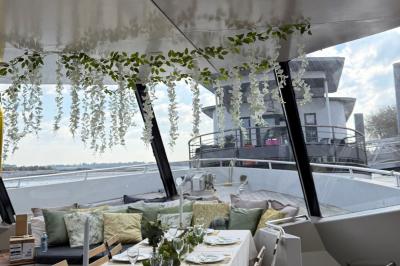 Mobilier en rotin noir avec coussins blancs sur une terrasse en bois couverte, vue sur l'extérieur urbain.