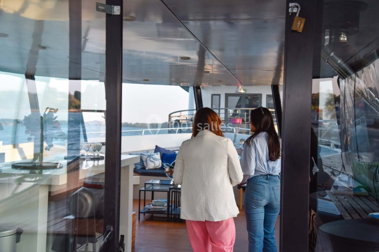 Deux femmes discutent à l'intérieur d'un bateau, avec vue sur un espace aménagé et l'eau à l'extérieur.