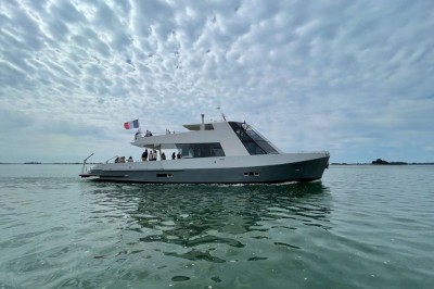 Mobilier en rotin noir avec coussins blancs sur une terrasse en bois couverte, vue sur l'extérieur urbain.