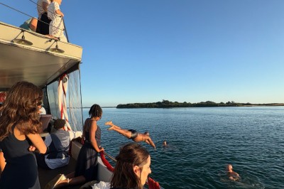 Vue depuis un bateau avec un siège orange au premier plan et un paysage côtier en arrière-plan.