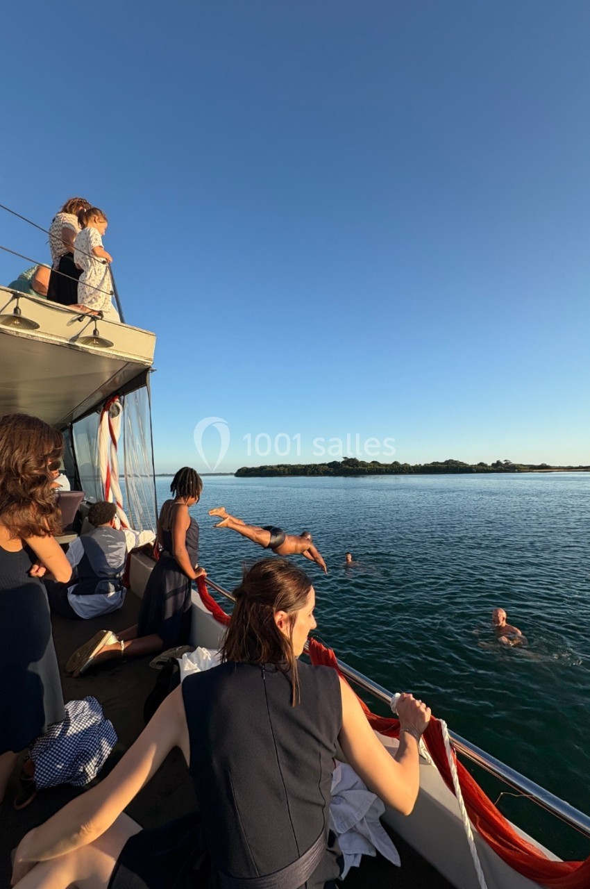 Des personnes sur un bateau observent ou participent à une baignade dans une eau calme au coucher du soleil.