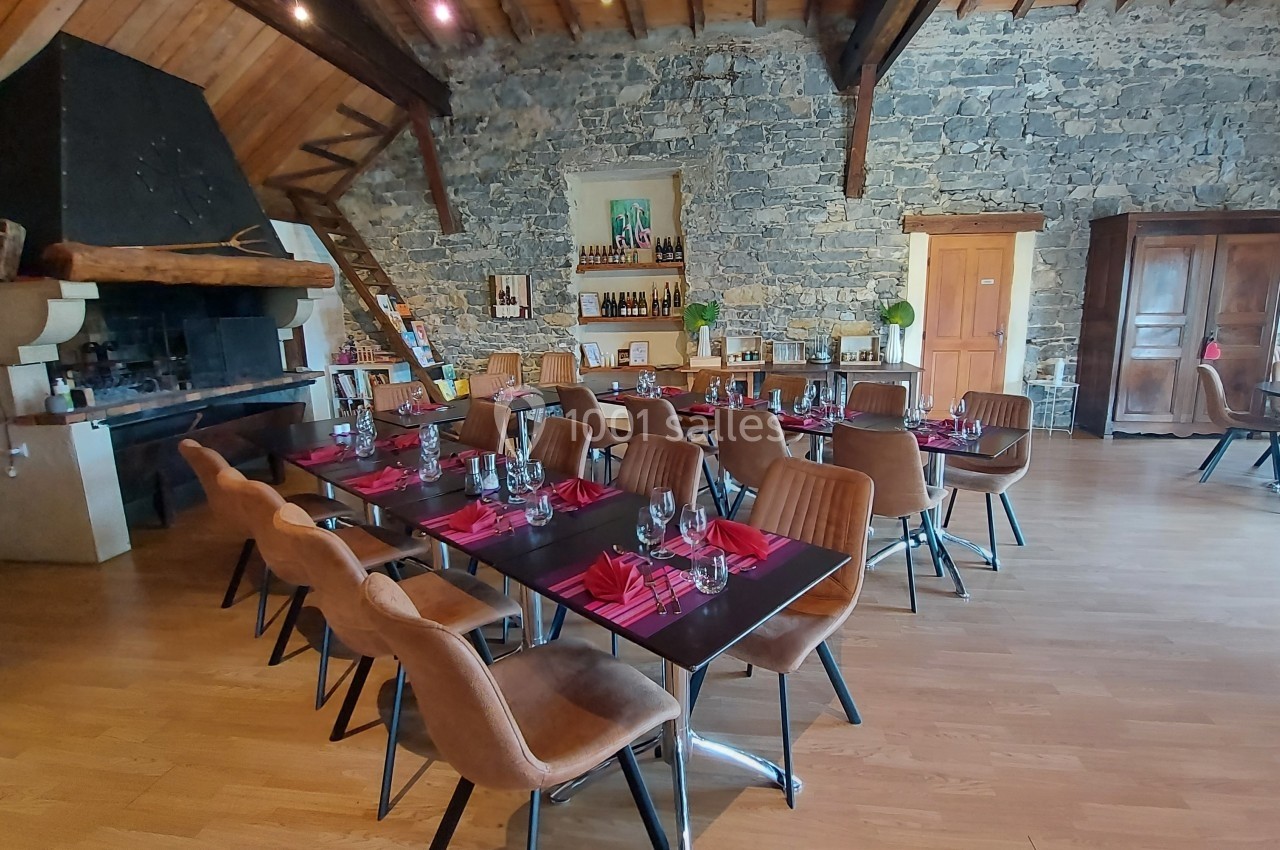 Location salle Quissac (Gard) - Le Mas de Roux #13 Salle de restaurant avec tables dressées, chaises en cuir, murs en pierre et cheminée rustique.