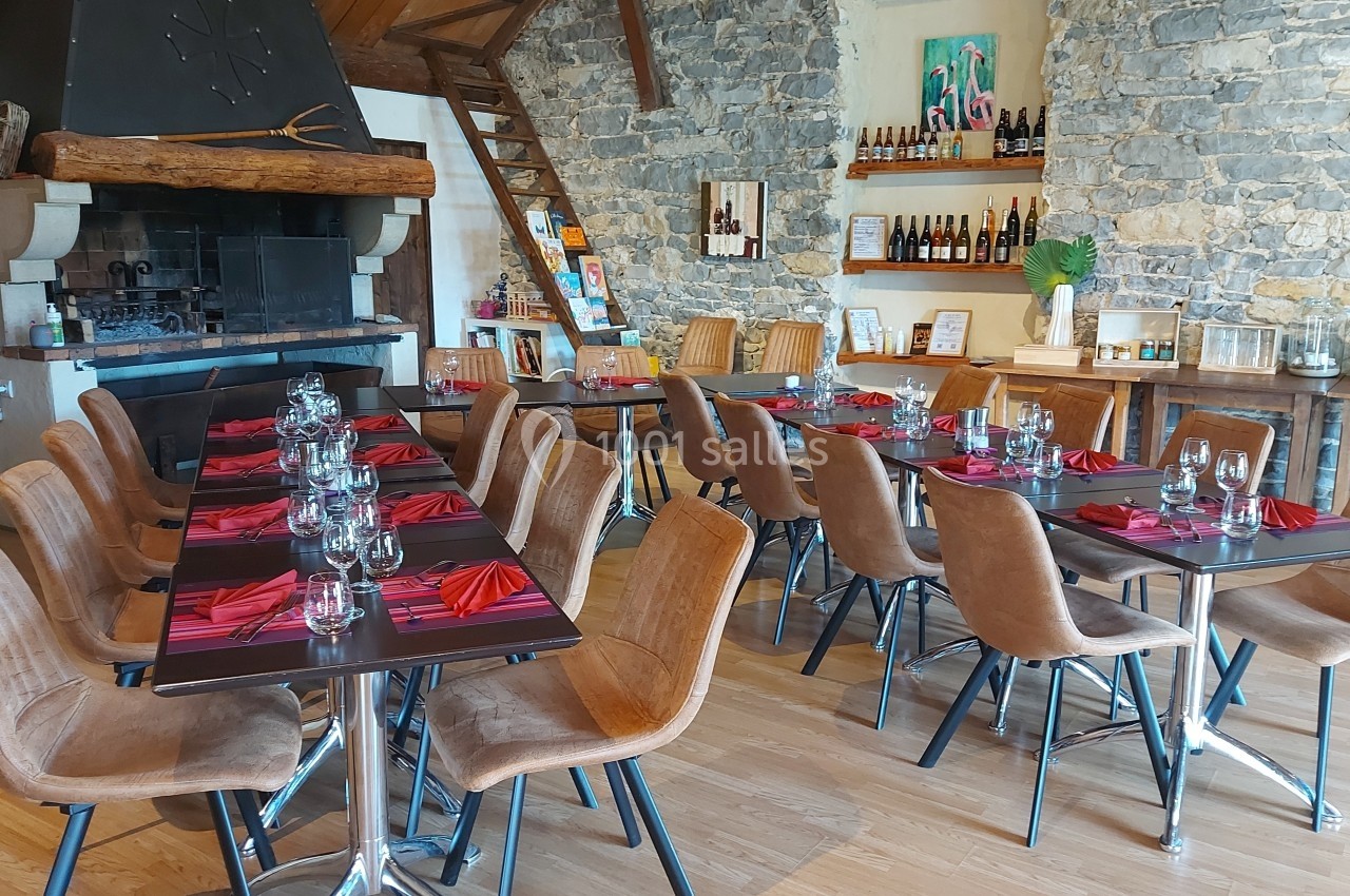 Location salle Quissac (Gard) - Le Mas de Roux #14 Salle de restaurant avec tables dressées, chaises en cuir, murs en pierre et cheminée décorative.
