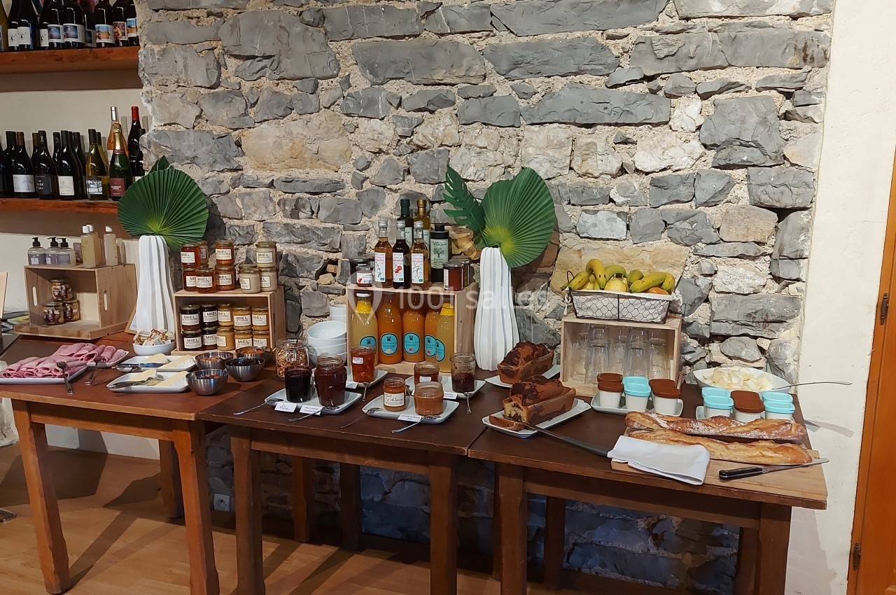 Location salle Quissac (Gard) - Le Mas de Roux #17 Buffet avec confitures, jus, viennoiseries, charcuteries et fruits, disposé sur des tables en bois devant un mur en pierre.