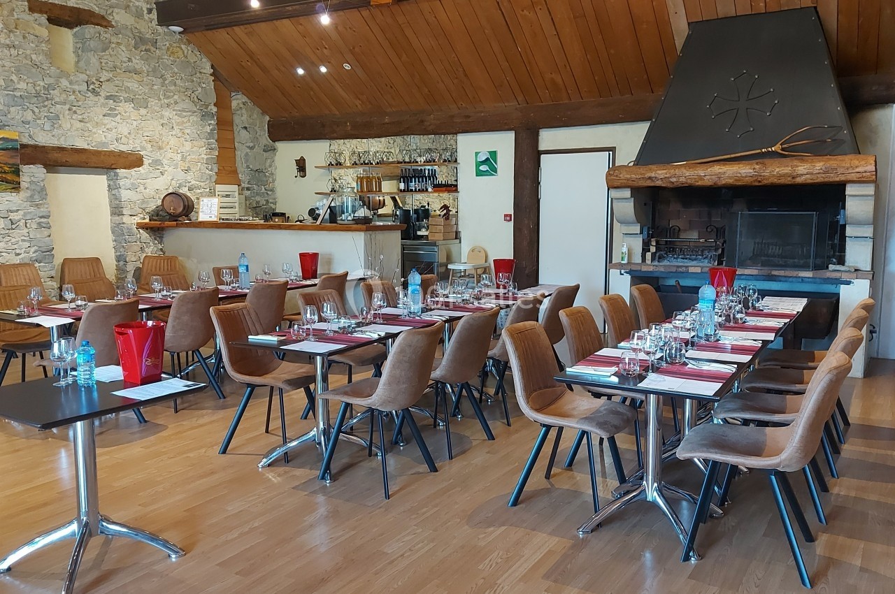 Location salle Quissac (Gard) - Le Mas de Roux #22 Salle de restaurant avec tables dressées, chaises en bois, cheminée en pierre et décor rustique.