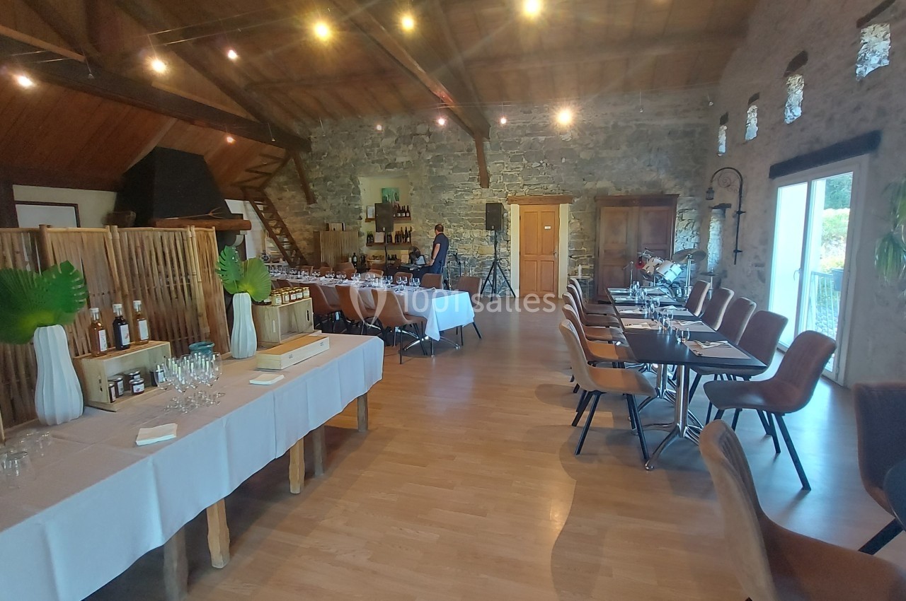 Location salle Quissac (Gard) - Le Mas de Roux #24 Salle de réception lumineuse avec tables dressées, murs en pierre apparente et plafond en bois.