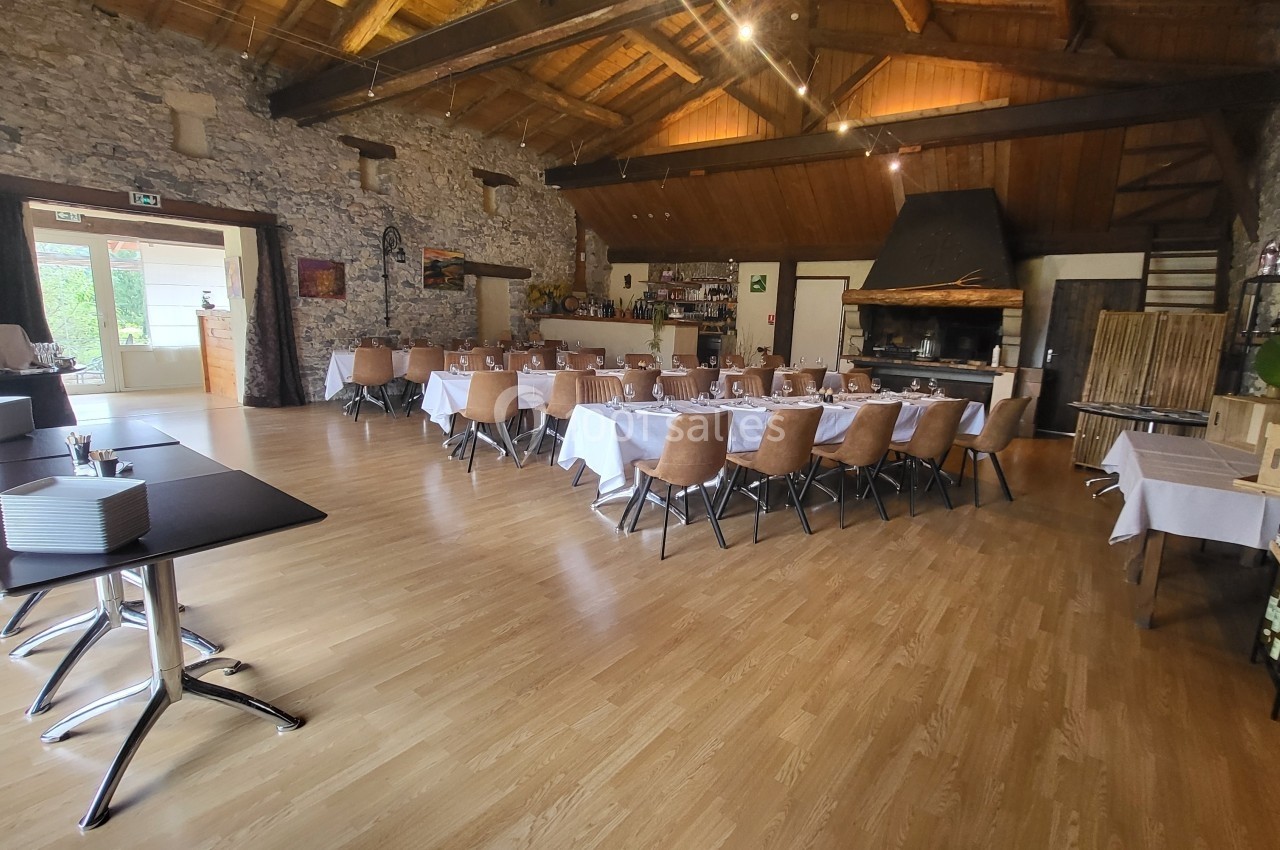 Location salle Quissac (Gard) - Le Mas de Roux #26 Salle de réception avec tables dressées, chaises en bois, murs en pierre et plafond en bois, éclairée par des lumières et…