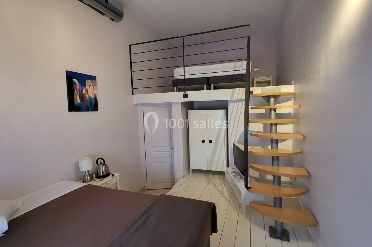Location salle Quissac (Gard) - Le Mas de Roux #34 Chambre avec lit double, mezzanine, escalier en colimaçon, armoire blanche et décoration murale colorée.