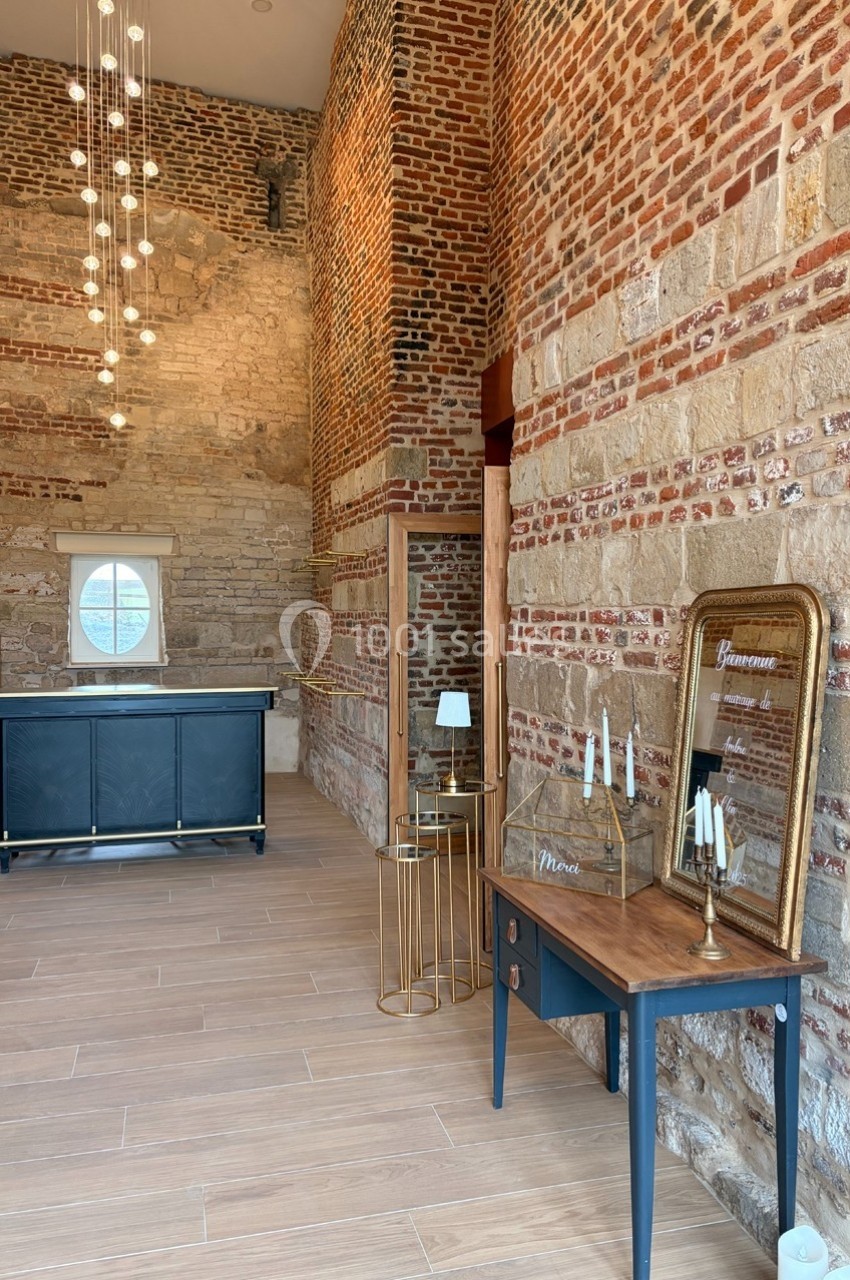 Salle en briques apparentes avec un comptoir, un miroir doré, une table en bois et un éclairage suspendu moderne.