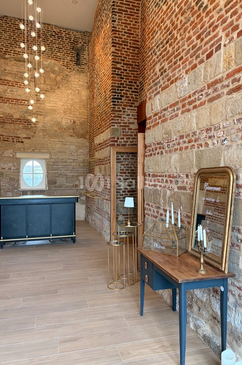 Salle en briques apparentes avec un comptoir, un miroir doré, une table en bois et un éclairage suspendu moderne.