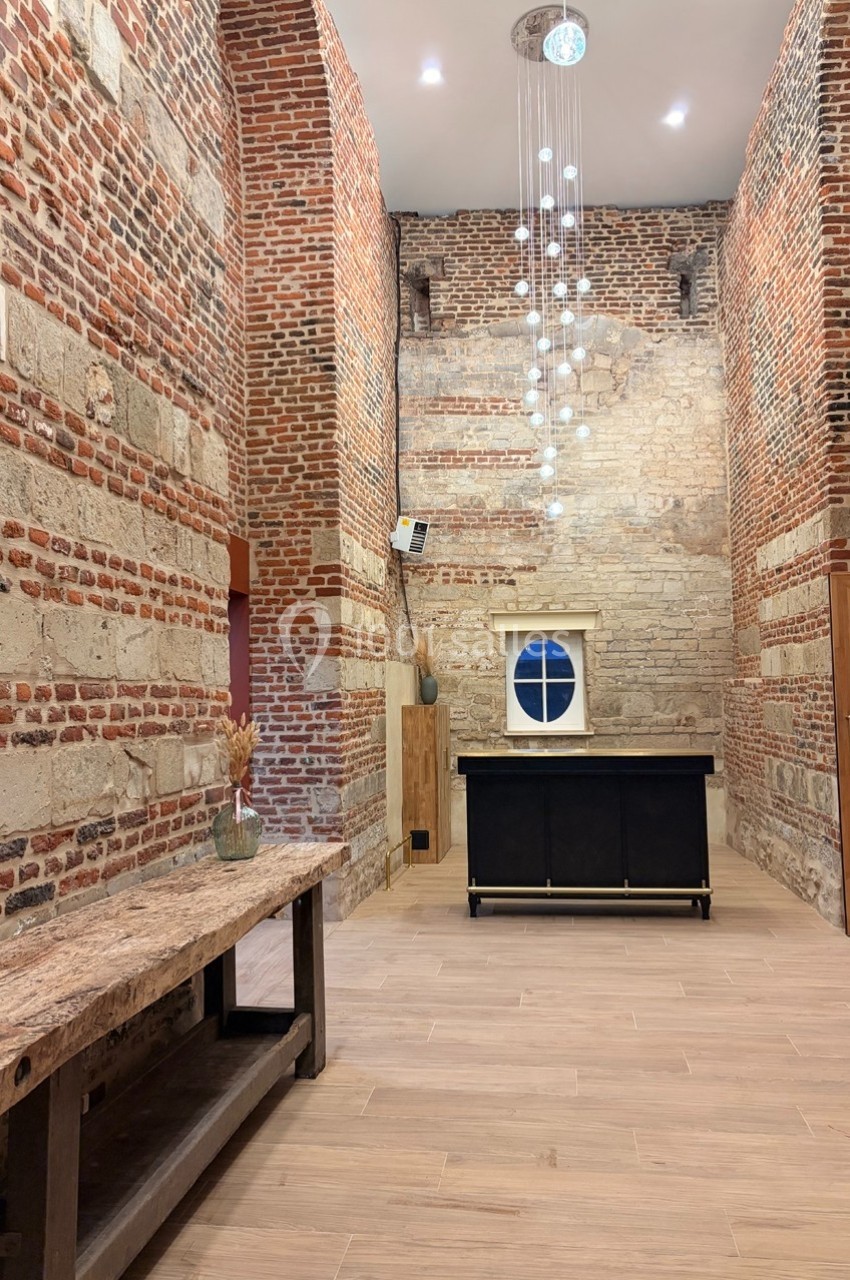 Salle en briques apparentes avec un plafond haut, un lustre moderne, un meuble noir et une table en bois rustique.