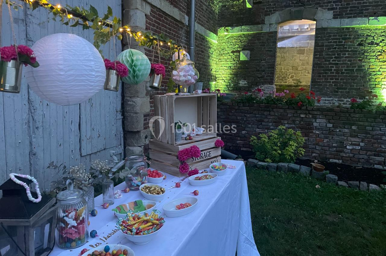 Table décorée pour un buffet de bonbons avec guirlandes lumineuses, pots en verre et éléments fleuris dans un jardin en…