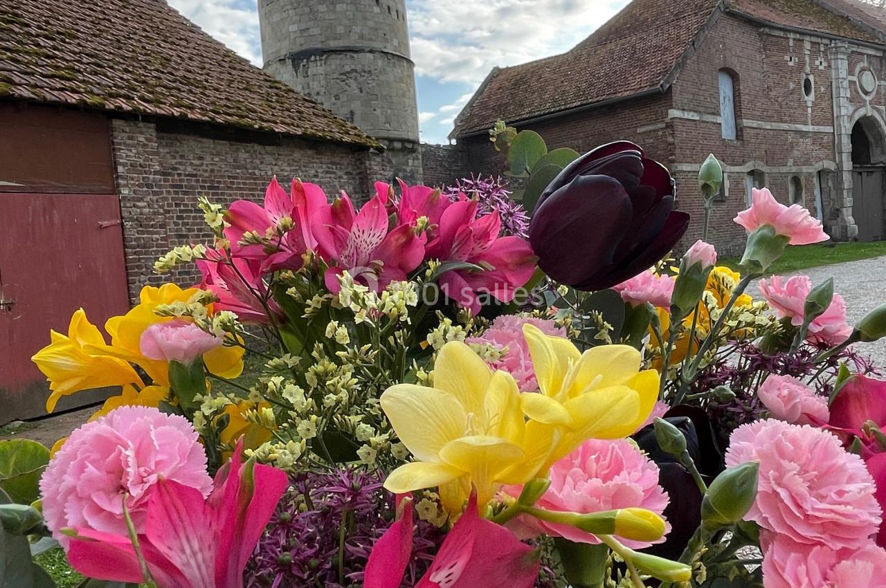 Bouquet de fleurs colorées au premier plan, avec une tour en pierre et des bâtiments en briques en arrière-plan.