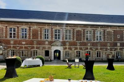 Miniature Cour intérieure du Château  Pièce rustique avec murs en pierre, plafond en bois, réservoir métallique rouge et mobilier simple.
