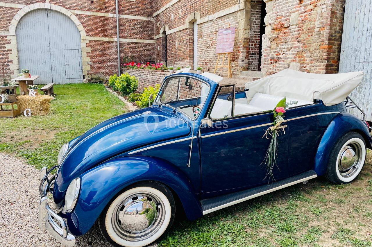 Voiture ancienne décapotable bleue garée devant un bâtiment en briques, décorée pour un événement festif.