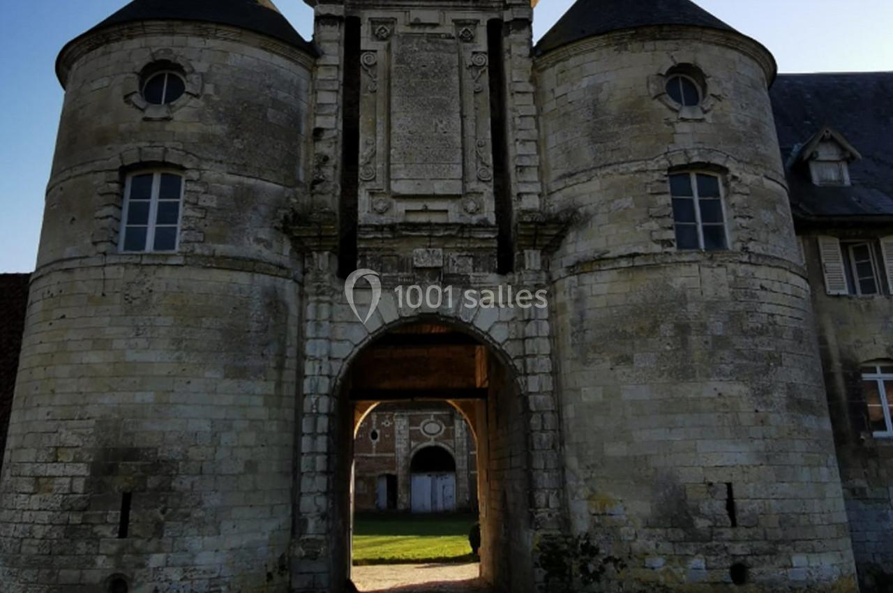 Porte monumentale en pierre avec deux tours rondes, donnant sur une cour intérieure éclairée par le soleil.