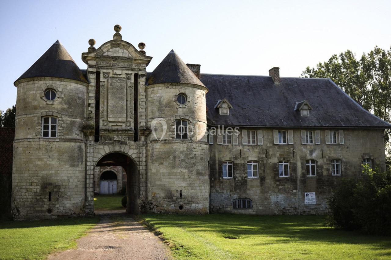 Façade d'un château ancien en pierre avec deux tours rondes, une arche centrale et un bâtiment attenant.