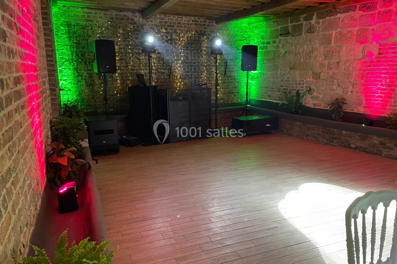 Salle en pierre avec éclairage coloré, parquet au sol, équipement audio et plantes décoratives.