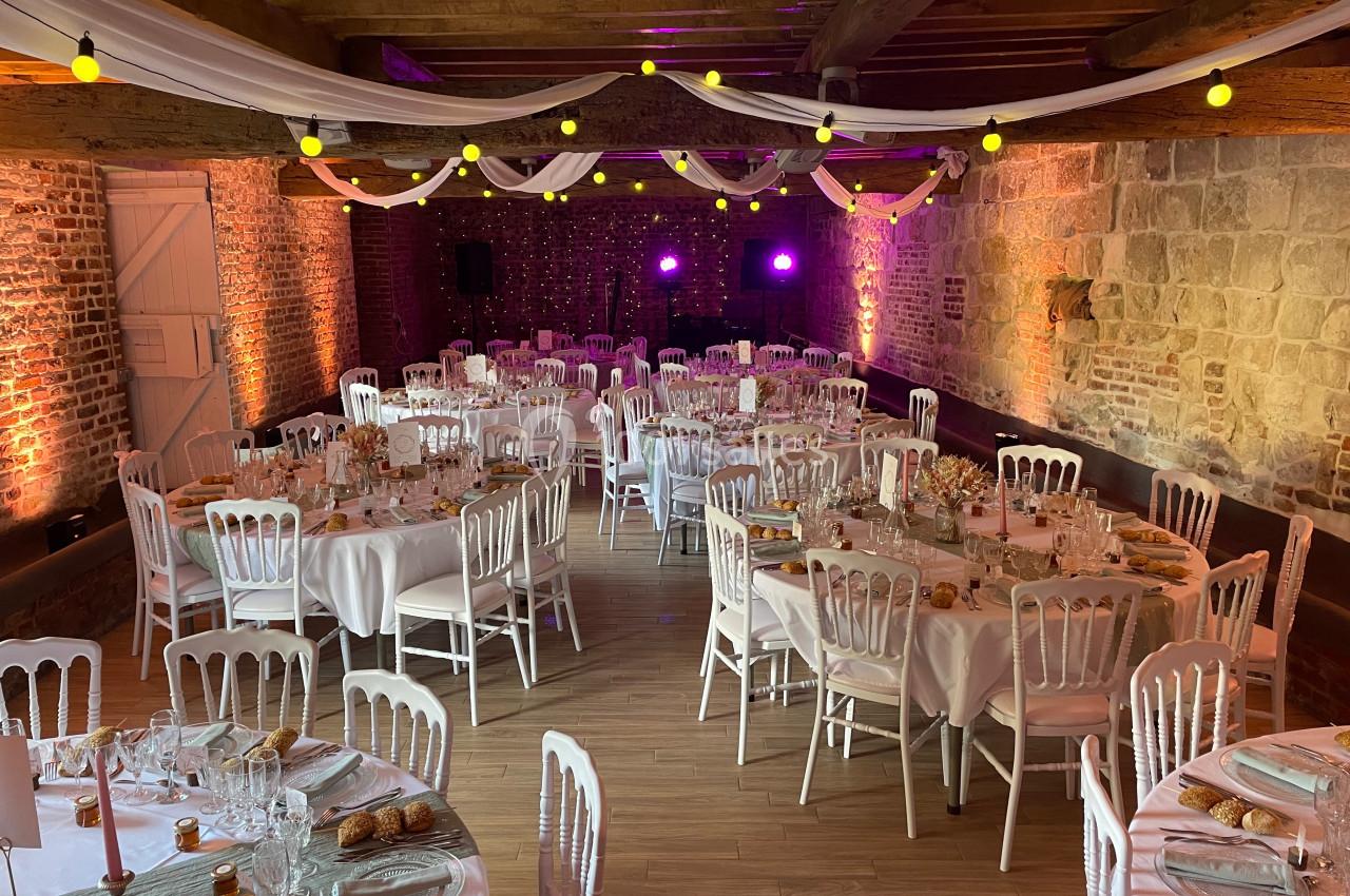 Salle de réception décorée avec des tables rondes, nappes blanches, chaises assorties et éclairage tamisé.