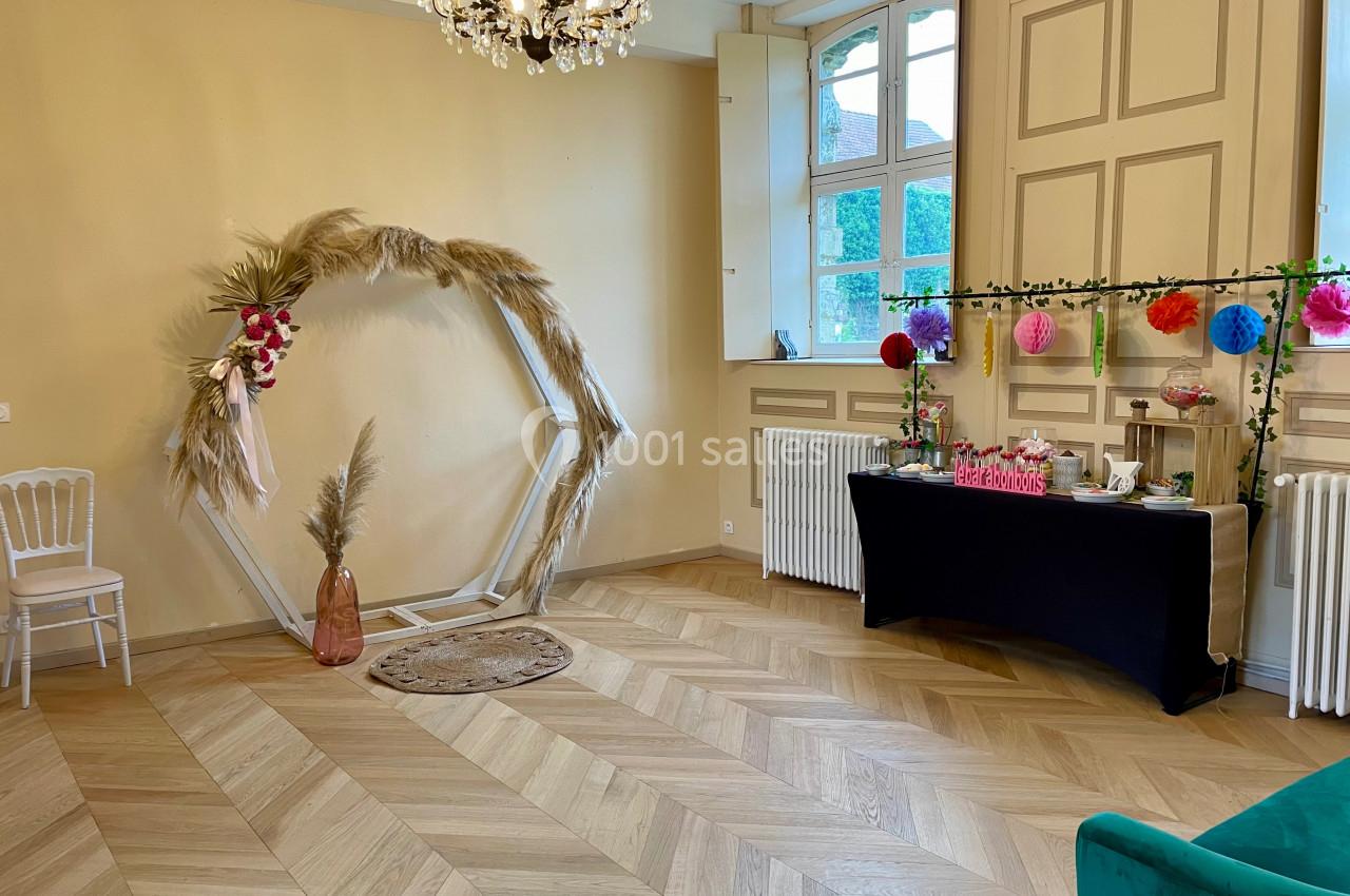 Salle décorée avec arche hexagonale ornée de fleurs et pampas, table de buffet avec décorations colorées et parquet en bois.