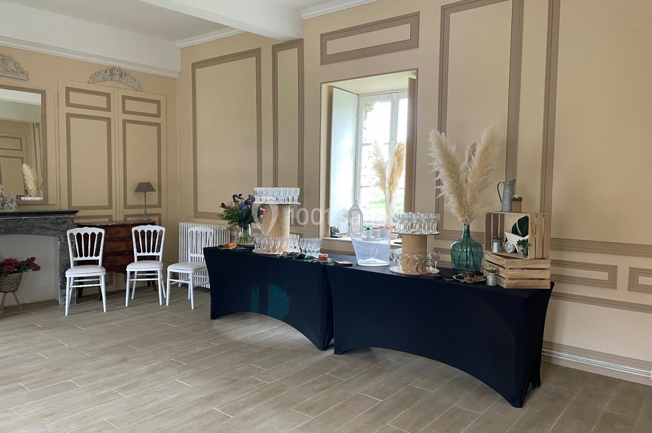 Salle élégante avec tables noires dressées pour un buffet, décorée de fleurs, pampas et caisses en bois près d'une fenêtre.