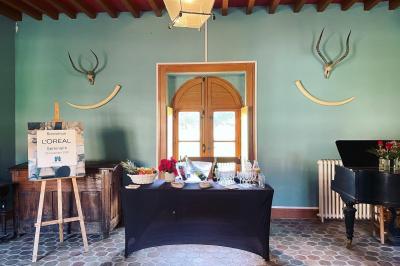 Miniature Salle d'entrée des salons Beaufremez  Pièce rustique avec murs en pierre, plafond en bois, réservoir métallique rouge et mobilier simple.