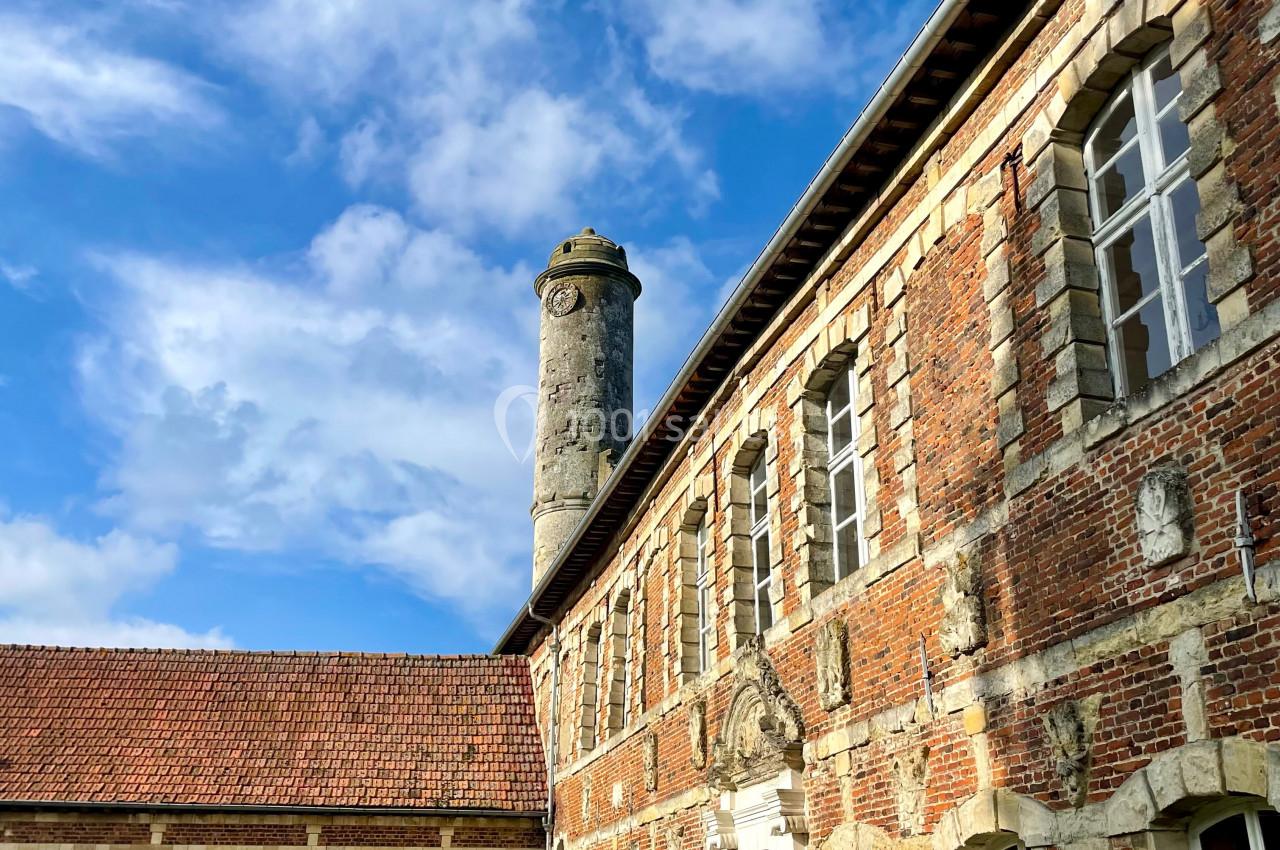 Bâtiment en briques rouges avec une tour en pierre, sous un ciel bleu parsemé de nuages.