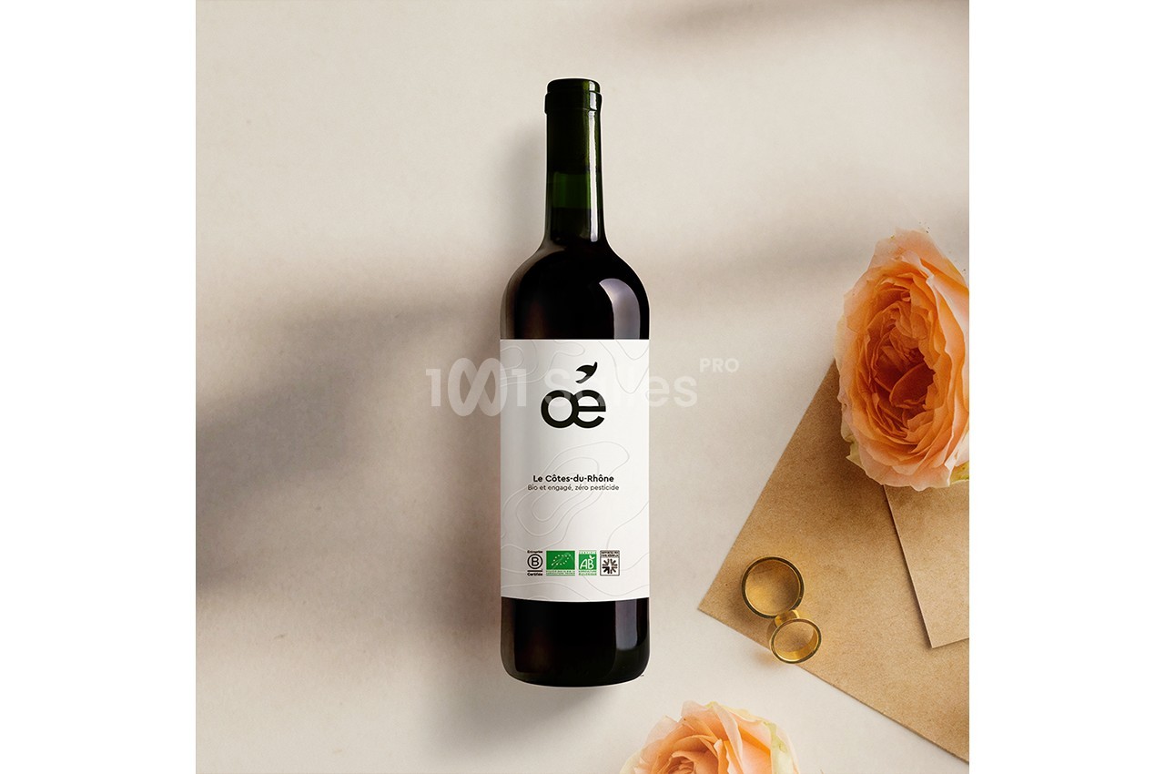 Bouteille de vin rouge posée sur une surface beige, accompagnée de roses orangées et d'une paire de lunettes dorées.
