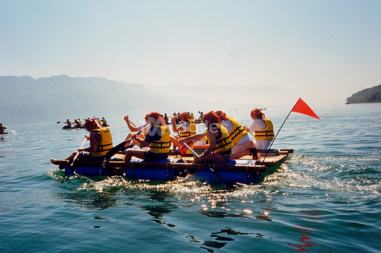 Des personnes en gilets de sauvetage pagaient sur un radeau improvisé sur un lac entouré de montagnes.