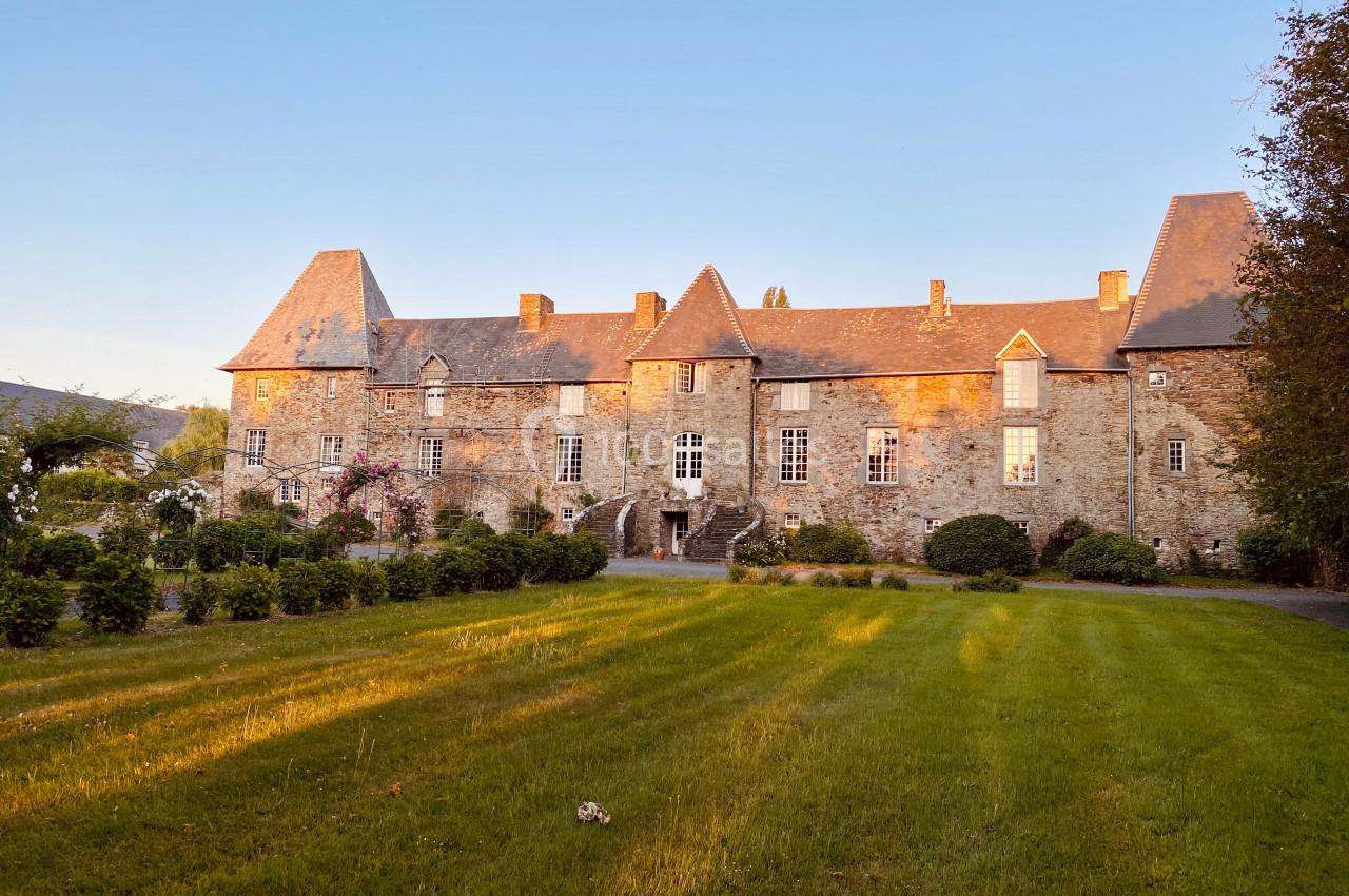 Façade d'un château en pierre entouré d'un jardin verdoyant sous une lumière de fin de journée.