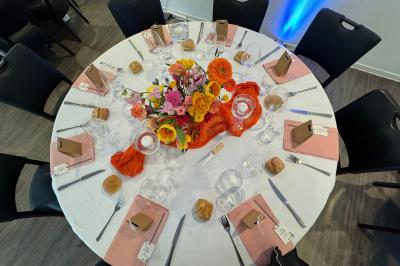 Miniature Location salle Bonneuil-sur-Marne (Val-de-Marne) - La Caravelle #17 Centre de table avec bougies torsadées, fleurs colorées et nappe orange, entouré de verres et couverts.