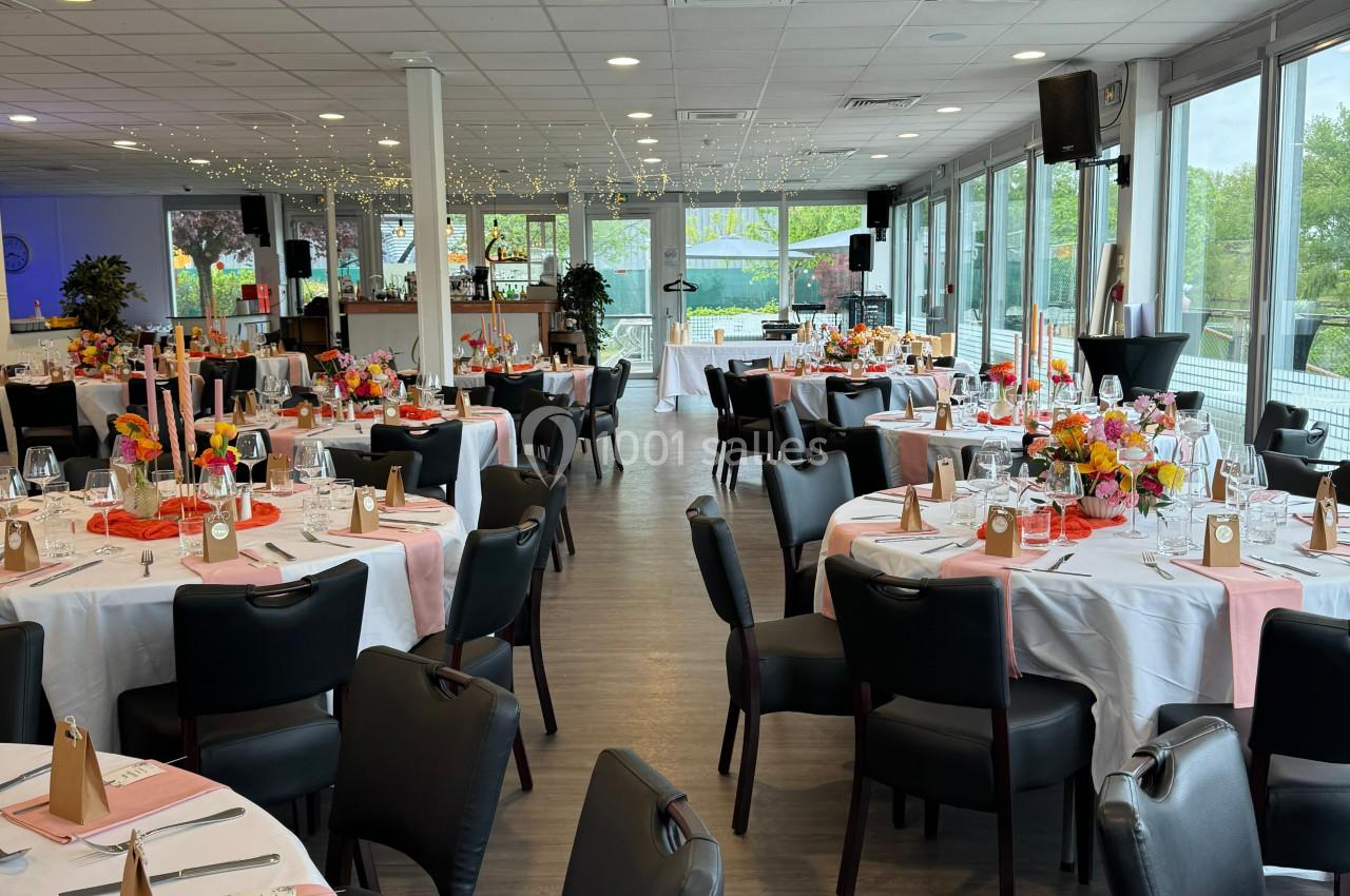Salle de réception élégamment décorée avec des tables rondes, nappes blanches et accents roses, prête pour un événement.