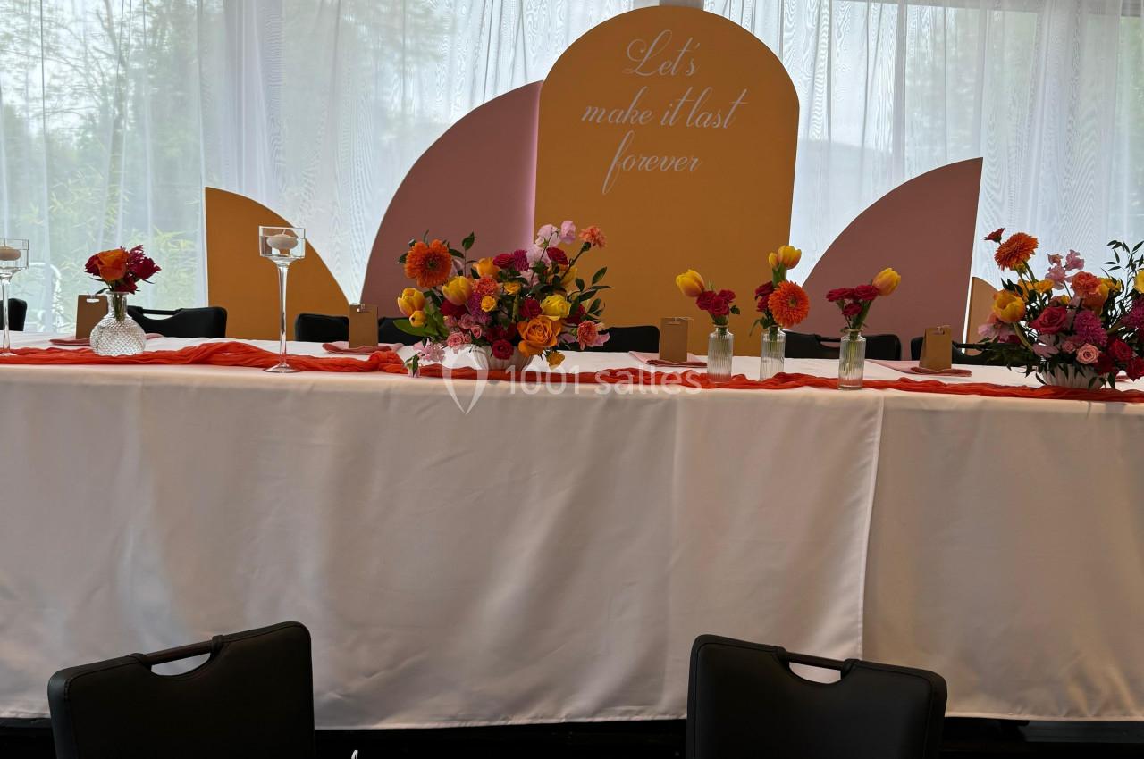 Table décorée avec des fleurs colorées et arrière-plan avec un panneau pastel portant un message en anglais.