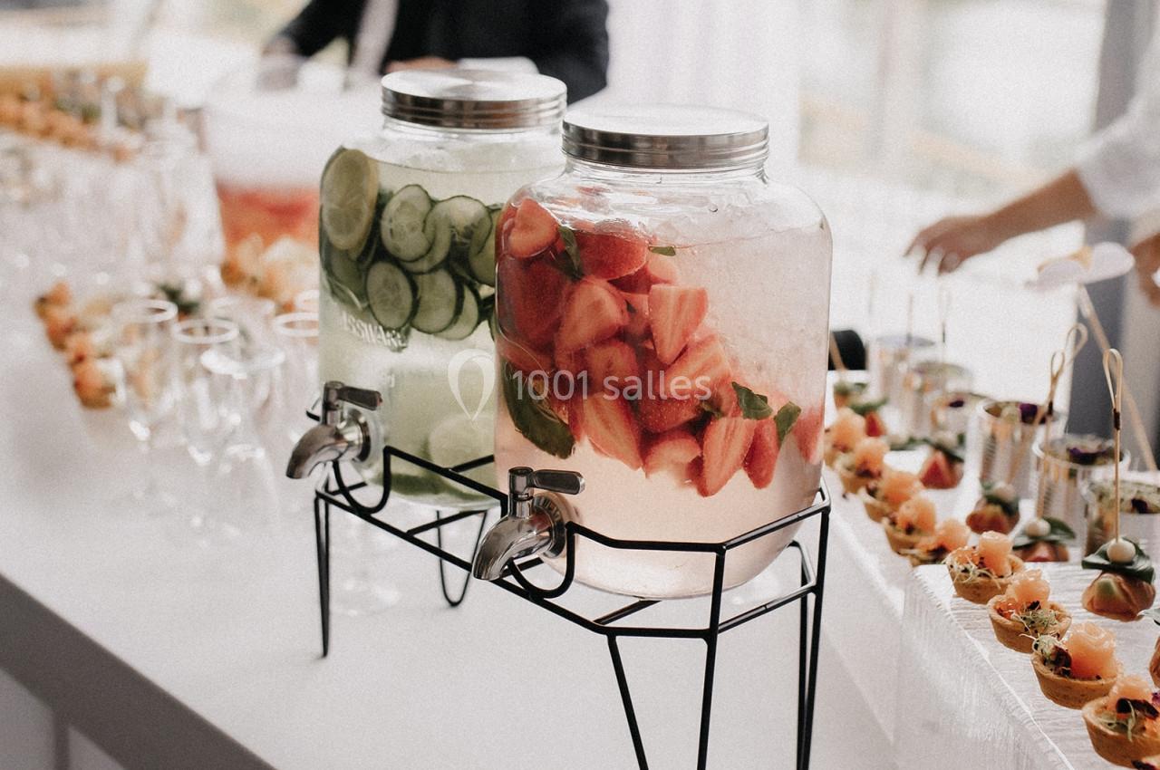 Deux distributeurs de boissons infusées, l'un aux concombres et l'autre aux fraises, sur une table de buffet.