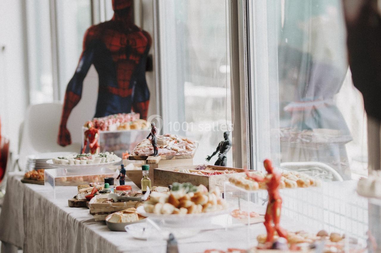 Table garnie de divers plats et desserts, décorée avec des figurines et une silhouette de super-héros en arrière-plan.