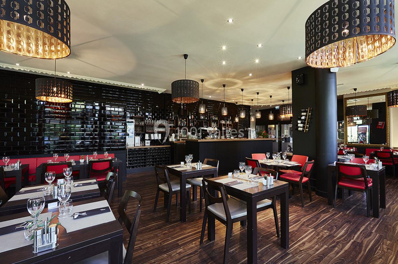 Salle de restaurant moderne avec tables dressées, chaises rouges et noires, éclairage chaleureux et décor élégant.